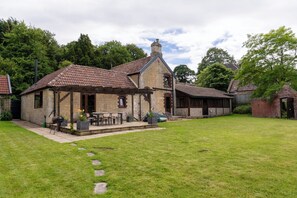 Un bâtiment en pierre avec un toit en tuiles, un patio couvert avec des meubles d’extérieur et une pelouse bien entretenue.