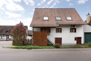 Ein zweistöckiges Haus mit Ziegeldach, einem Holztor und einem kleinen Garten.