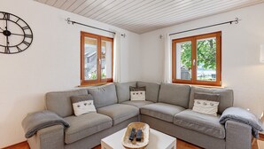 Una sala de estar con un sofá seccional, una mesa de centro, un reloj de pared y dos ventanas con cortinas.