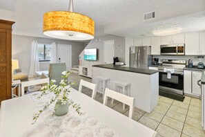 A modern kitchen with white cabinets, stainless steel appliances, a central island, and a dining area with a table and chairs. - New Listing! Cozy 2 bed 1.5 bath at Gulf Highlands (Panama City Beach)