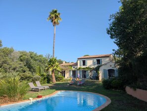 A pool with lounge chairs, a tall palm tree, and a building with a tiled roof.