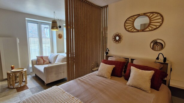 A bedroom with a bed, a sofa, a bedside table with a candle, a window, and a wall with decorative items. - Cosy, quiet studio in the historic center of Senlis (Senlis)