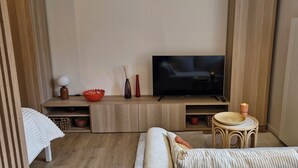 A cozy living room with a flat-screen TV, wooden furniture, a small round table, and a comfortable sofa. - Cosy, quiet studio in the historic center of Senlis (Senlis)