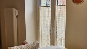 A dining area with a table set for two, chairs, a hanging light fixture, and a window with a view of buildings. - Cosy, quiet studio in the historic center of Senlis (Senlis)