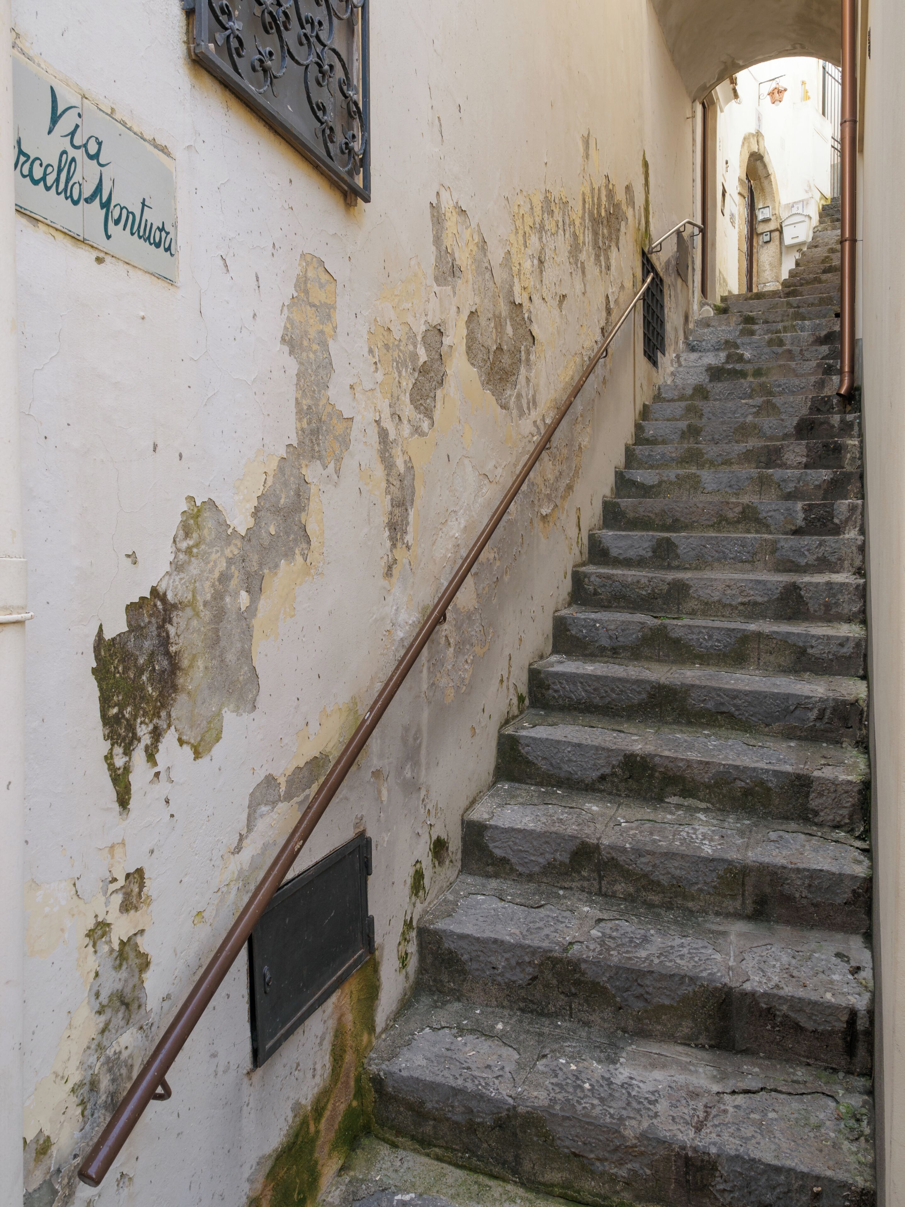 A staircase with peeling wall paint and a metal handrail.