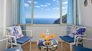 A room with a view of the sea, two chairs with cushions, a table with a bottle and glasses, and a plate of food. - De Vivo Realty - La casa del Cavaliere (Positano)