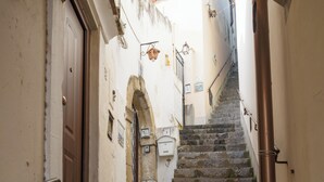 A narrow stairway leading to a door, with a metal handrail on the left and a wall-mounted light fixture above. - De Vivo Realty - La casa del Cavaliere (Positano)