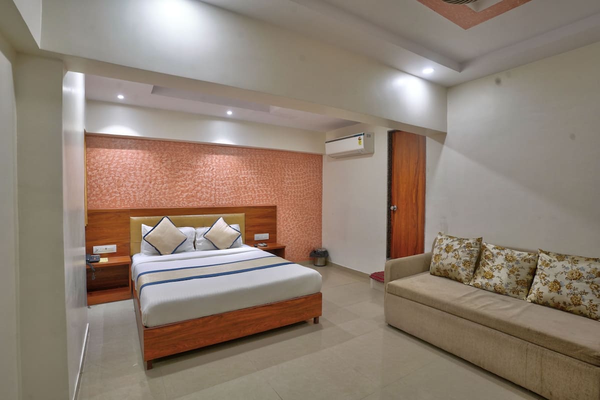 A hotel room with a bed, a sofa, a nightstand, an air conditioning unit, and a wall with a patterned design.