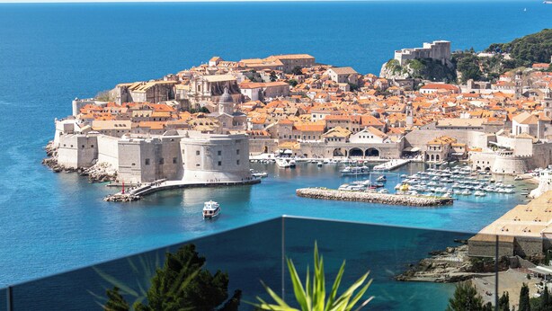 A balcony with lounge chairs overlooking a coastal town with historic buildings and a clear blue sea. - DUBROVNIK VISTA RESIDENCE by DuHomes  (Dubrovnik)