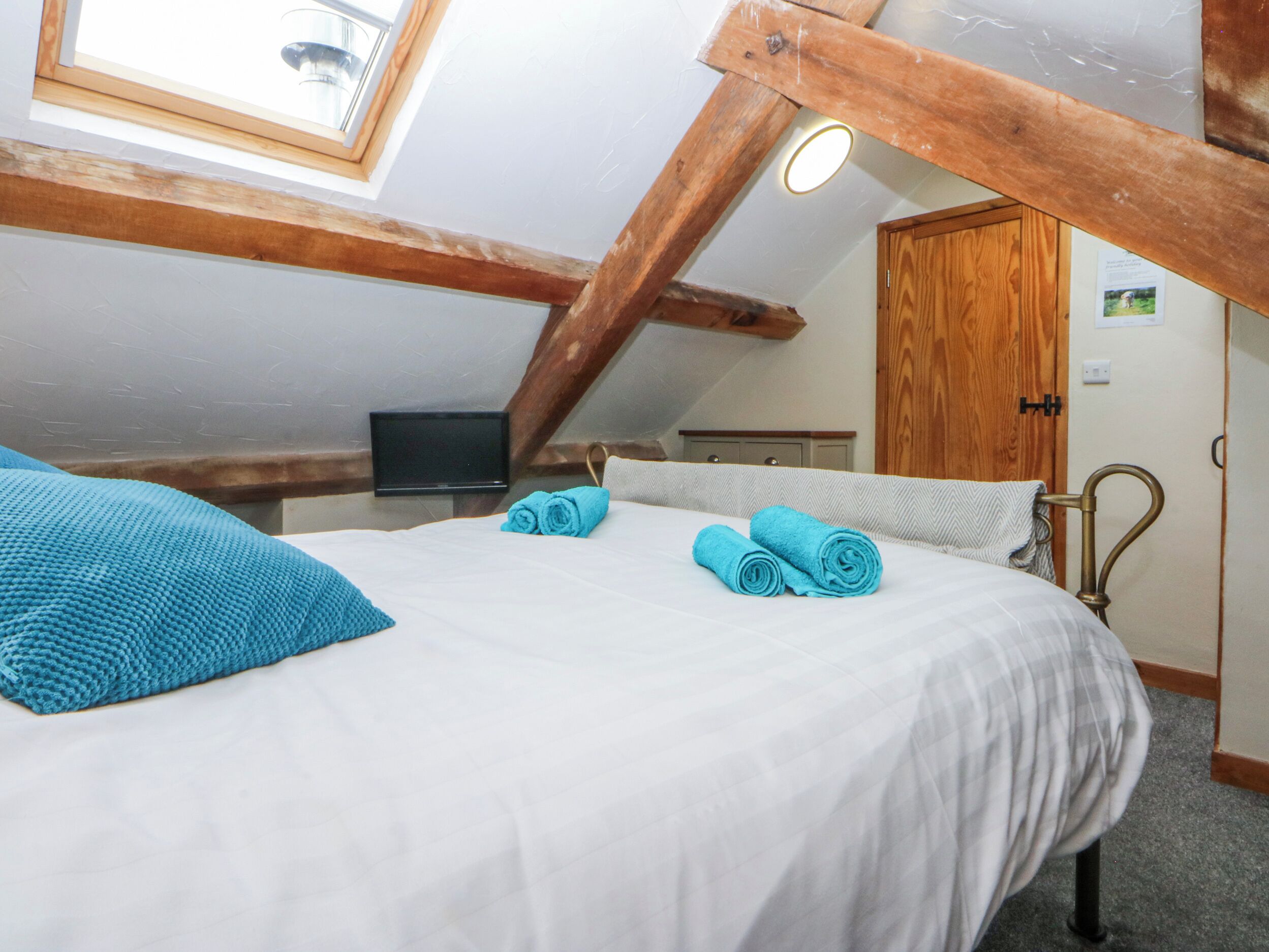 A bedroom with a bed, rolled towels, a television, and a wooden ceiling structure.