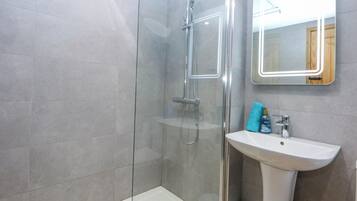 Un baño moderno con ducha envuelta en vidrio, un lavabo blanco y un espejo con marco iluminado.