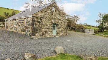 A stone building with a sloped roof, a green door, and a gravel driveway.