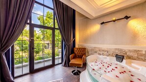 A room with a large window, a leather armchair, a bathtub with rose petals, and a wall-mounted light fixture. - White Mansion Cappadocia (Nevşehir)