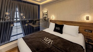 A modern hotel room with a large bed, a glass partition, and a view of the outdoors. - White Mansion Cappadocia (Nevşehir)