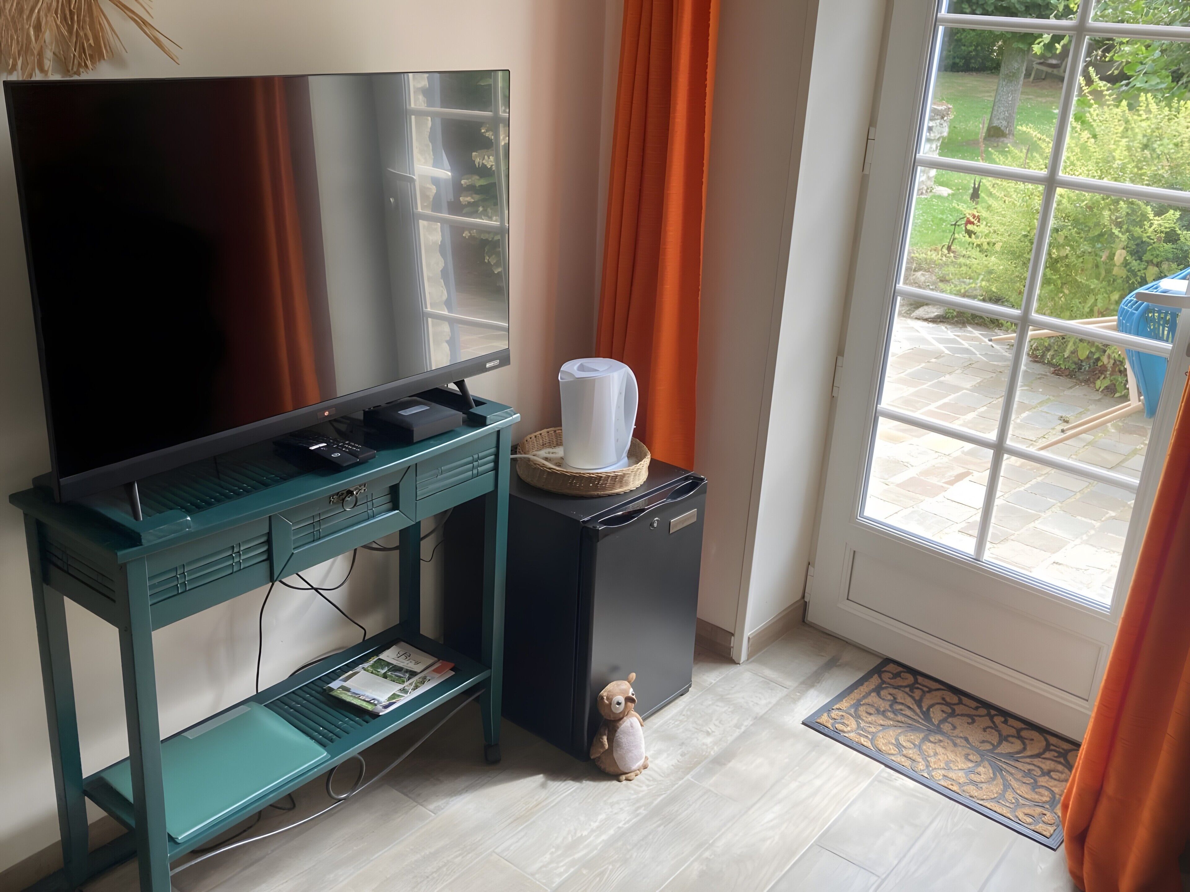 A teal desk with a flat-screen TV, a coffee maker, and a small bear figurine.