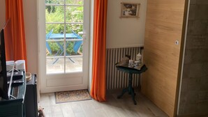 Une pièce avec une porte donnant sur un balcon, une petite table avec une tasse et une soucoupe, un ventilateur de plafond en osier et un panneau mural en bois.