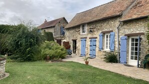 Un bâtiment en pierre avec un toit en tuiles, une cour pavée et une zone herbeuse.