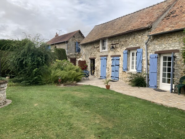 Un bâtiment en pierre avec un toit en tuiles, une cour pavée et une zone herbeuse.