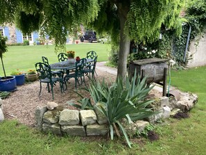 Un jardin avec une table et des chaises, un mur en pierre et un arbre.