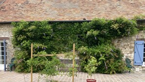 Un bâtiment en pierre avec un toit en tuiles, une pergola en bois et un pot de fleurs.
