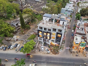 Vista aérea de un edificio de varios pisos con un estilo arquitectónico moderno, rodeado de coches estacionados y una calle concurrida.