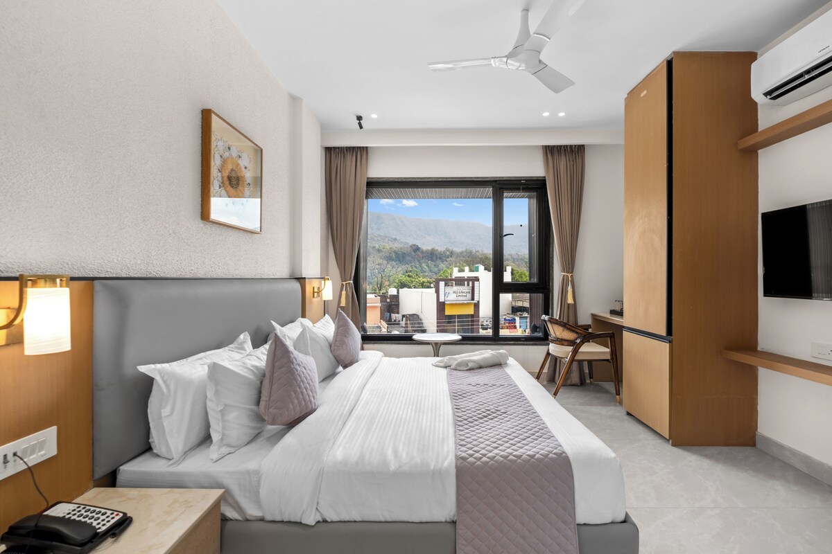 Ein Hotelzimmer mit Bett, Nachttisch, Lampe und Blick auf einen Berg.