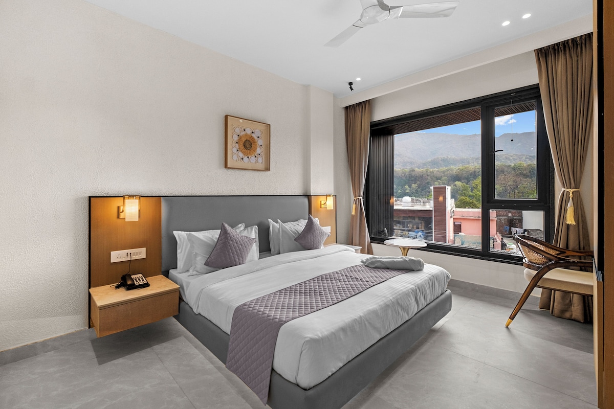 Ein Hotelzimmer mit einem großen Bett, Nachttischlampen, einem Nachttisch, einem Schreibtisch und einem Fenster mit Bergblick.
