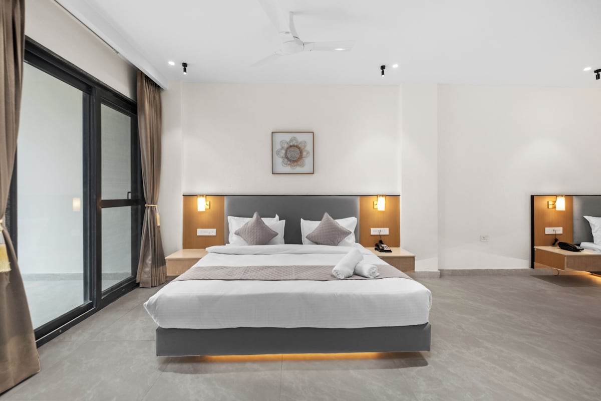 Ein modernes Hotelzimmer mit einem großen Bett, Nachttischen, einem Deckenventilator und einem großen Fenster mit Vorhängen.