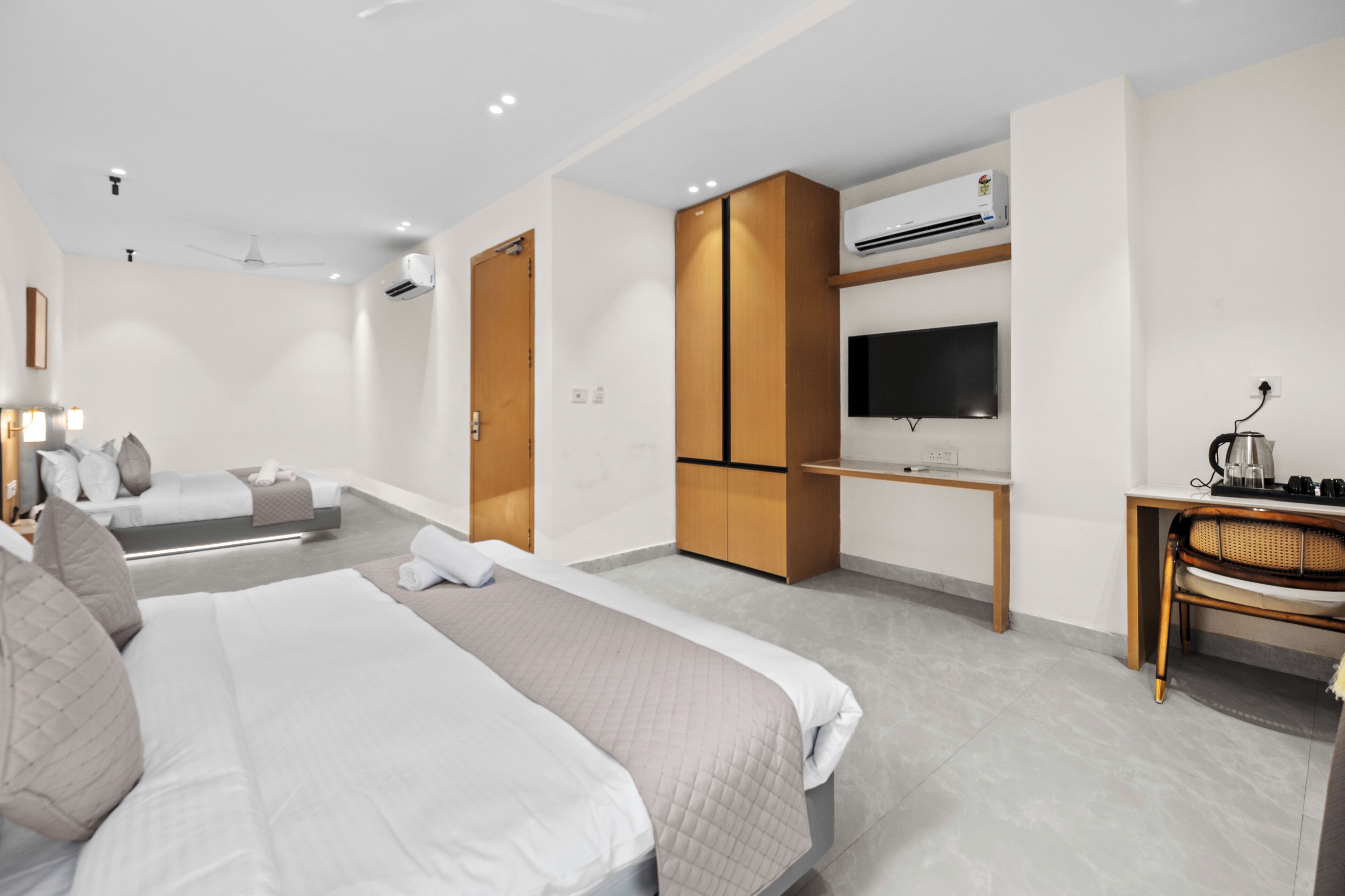 A modern hotel room with a large bed, a desk, a television, and an air conditioning unit.