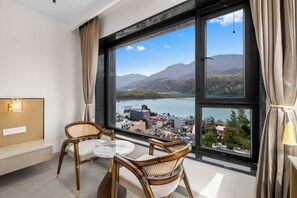 Ein Zimmer mit großem Fenster, zwei Korbstühlen, einem kleinen runden Tisch und einer hölzernen Bank.