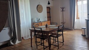 Un coin repas avec une table et des chaises en bois, une horloge au mur et un porte-manteau.