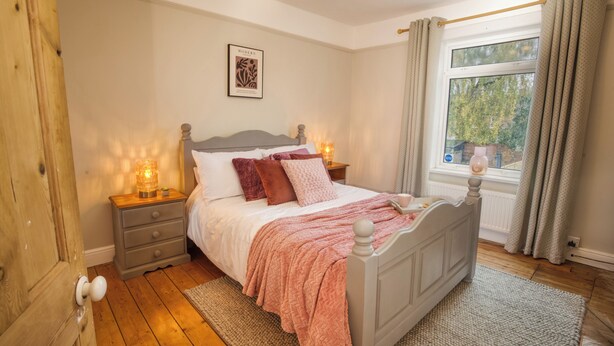 Ein Schlafzimmer mit einem Bett, Nachttischen, einem Fenster mit Vorhängen und einem Wandbild.