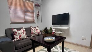 Una sala de estar con un sofá, una mesa con un cuenco, una televisión y una ventana con persianas.