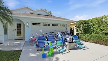 A house with a garage, a driveway, and several blue and white beach chairs and a pink bicycle.