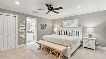 A bedroom with a bed, bedside tables, a bench, a ceiling fan, and a door leading to a bathroom.