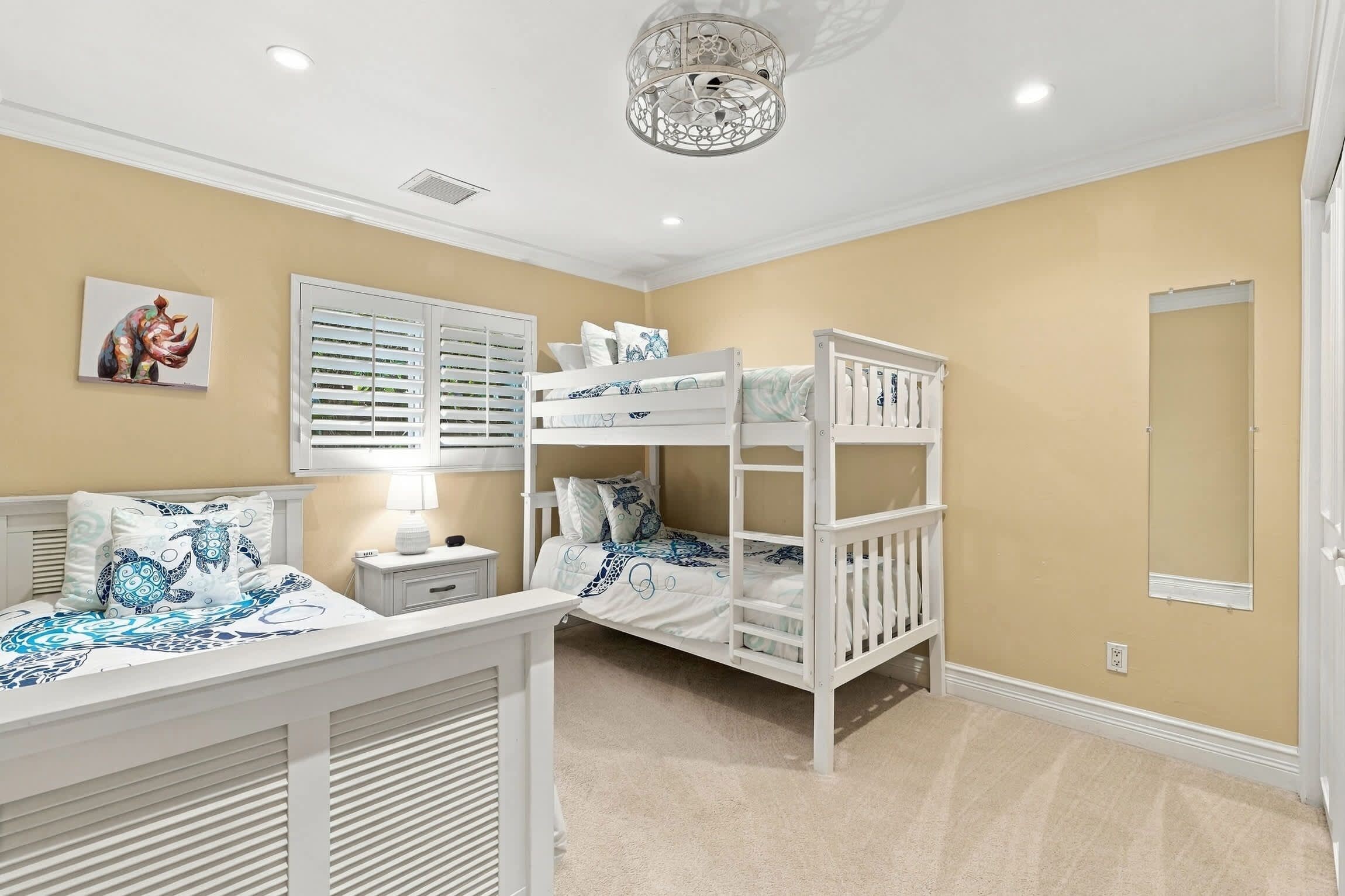 A bedroom with bunk beds, a bedside table, a lamp, a ceiling light fixture, and a wall-mounted picture.