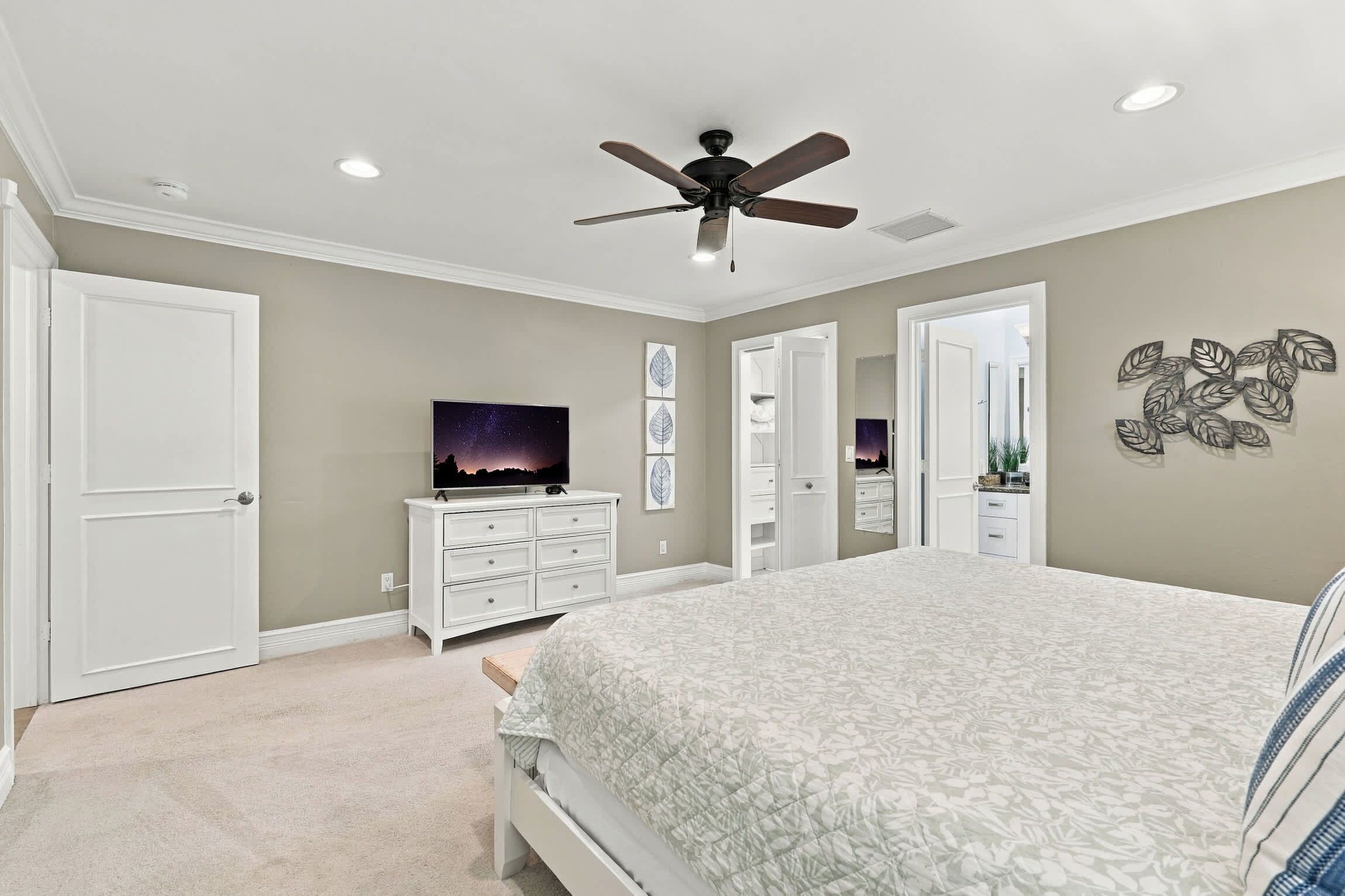 A bedroom with a bed, a ceiling fan, a dresser, a television, and a door.