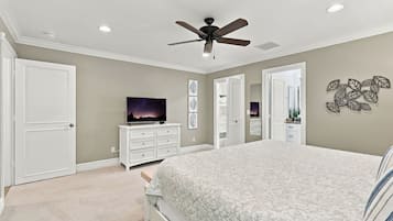 A bedroom with a bed, a ceiling fan, a dresser, a television, and a door.