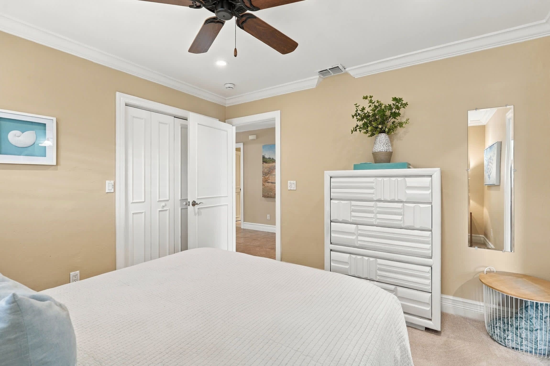 Un dormitorio con cama, armario, ventilador de techo y puerta que da a otra habitación.