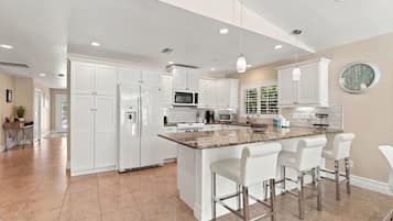 A modern kitchen with white cabinetry, a central island with bar stools, and a large window with a view of greenery.