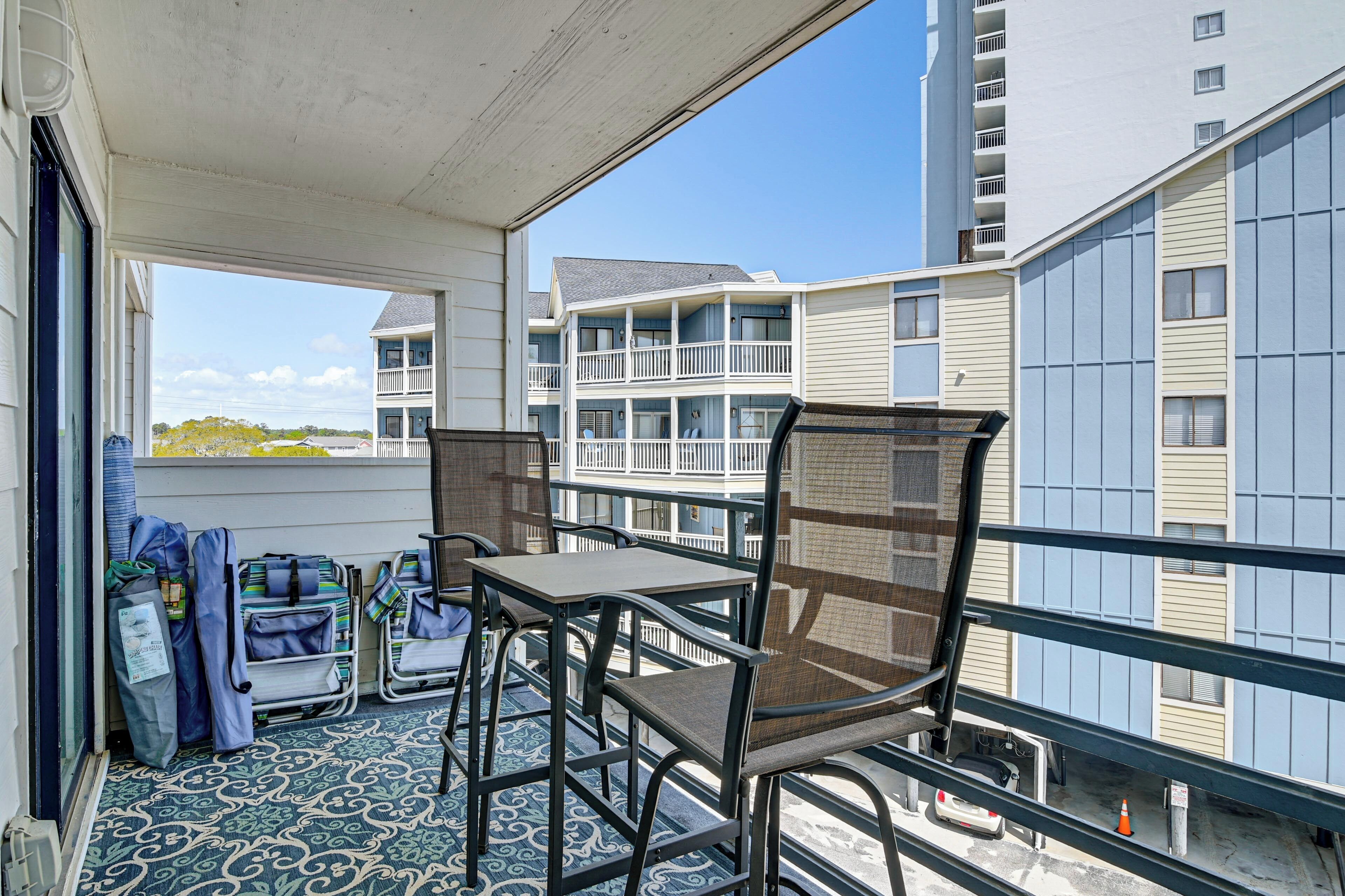 A balcony with a table and chairs, luggage, and a view of multi-story buildings.