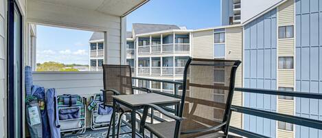 A balcony with a table and chairs, luggage, and a view of multi-story buildings.