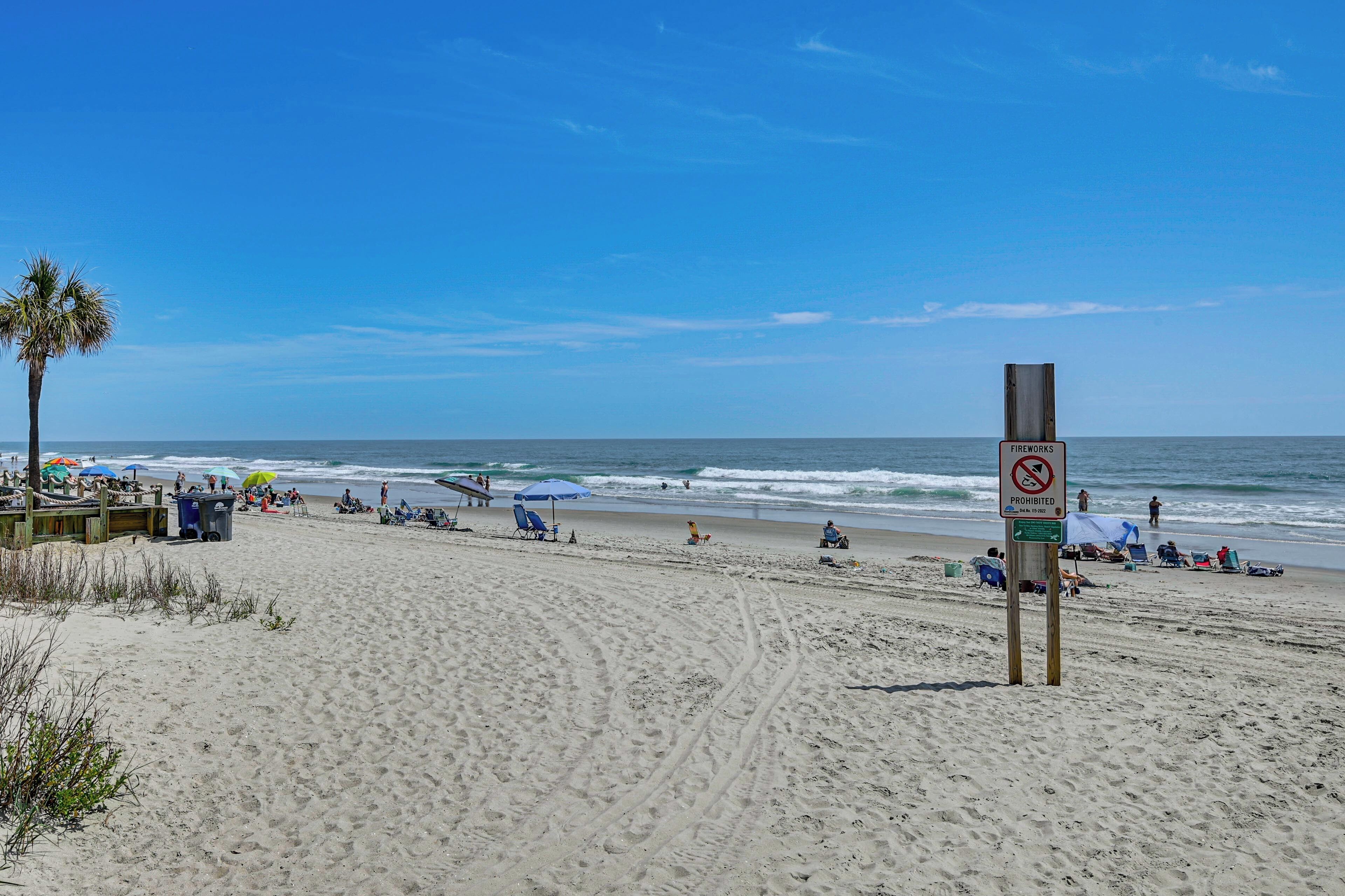 A beach with a sign indicating no swimming, a wooden structure, and people relaxing on the sand.