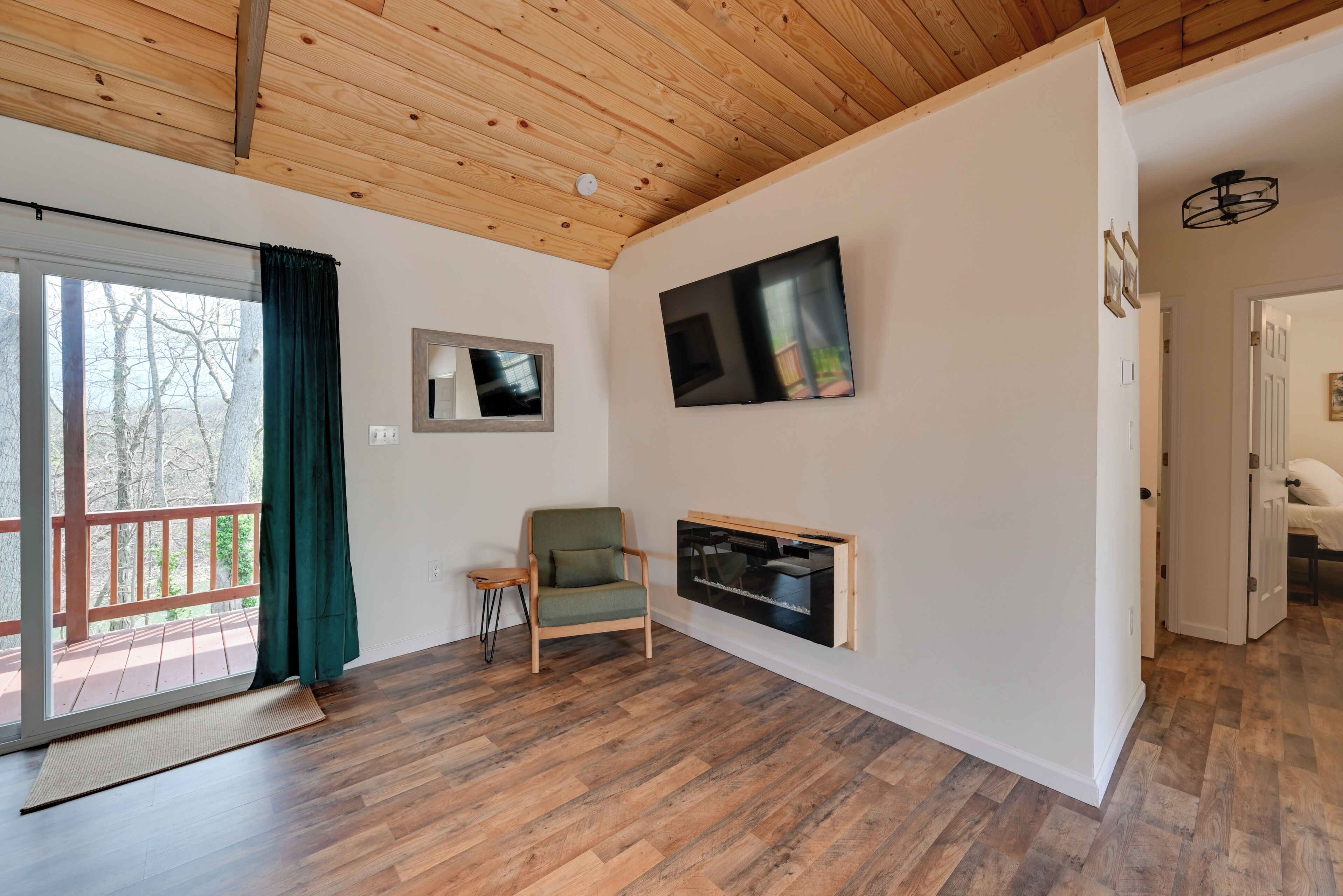 A room with a wooden ceiling, a sliding glass door, a green chair, a flat-screen TV, and a small table.