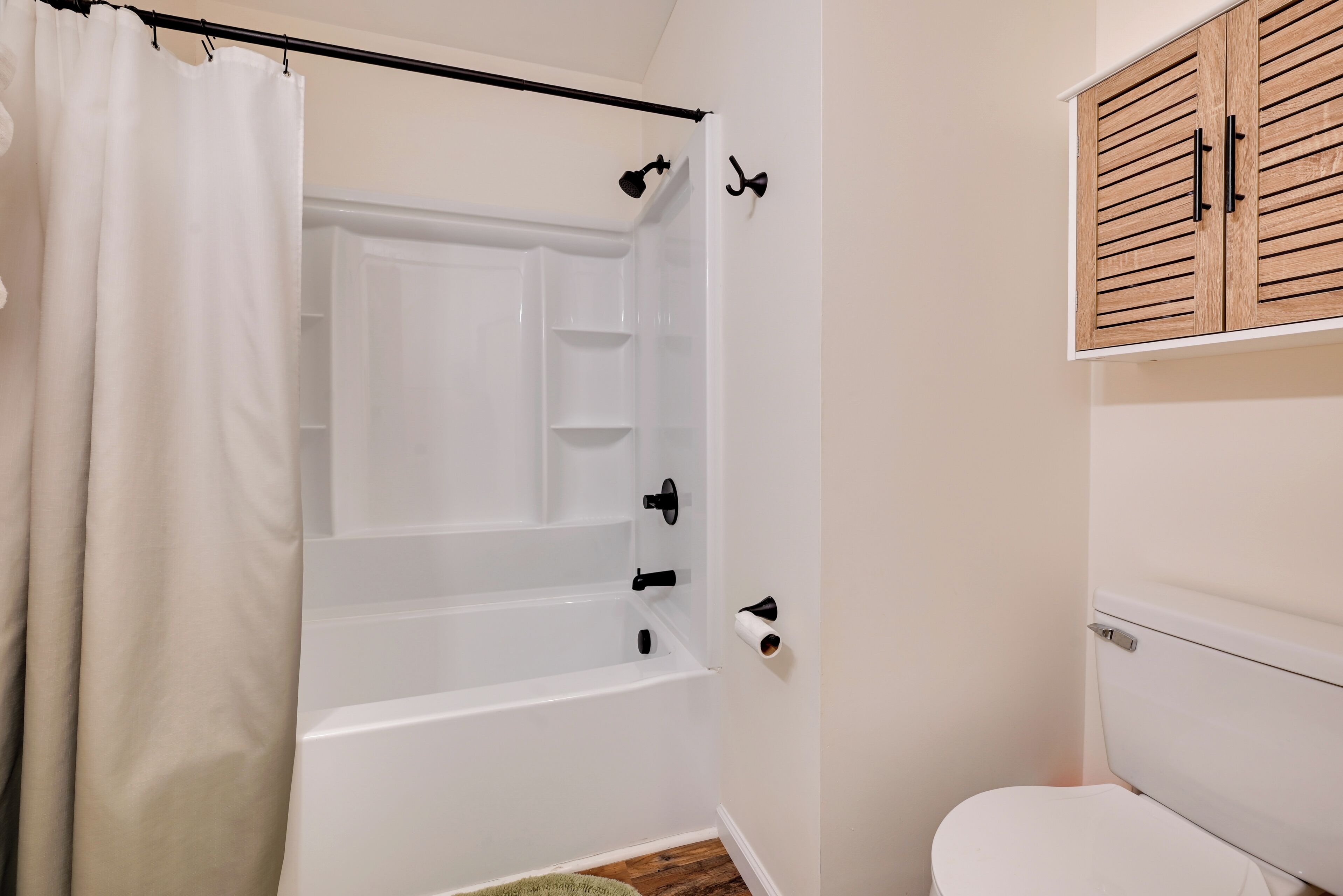A bathroom with a bathtub, toilet, and wooden cabinet.