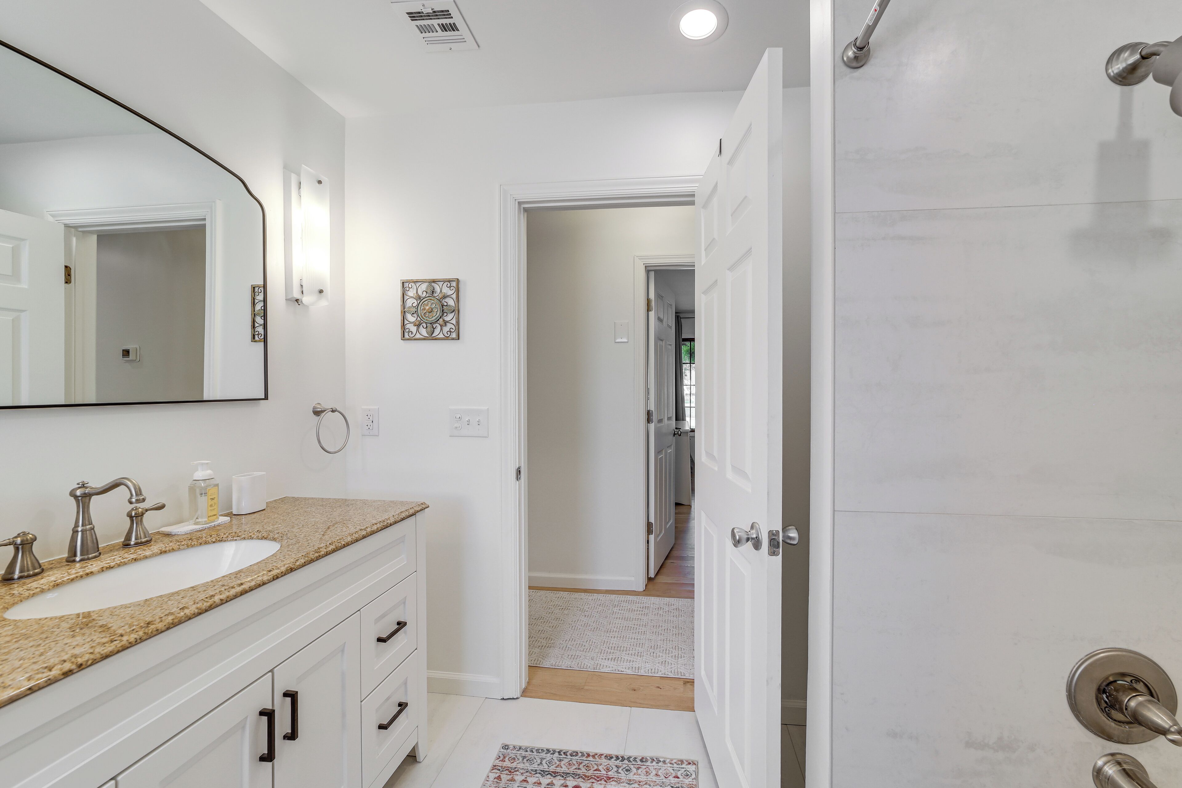 A bathroom with a white sink, a large mirror, and a door leading to another room.