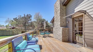 Una terraza de madera con mobiliario exterior, un muro de piedra y una puerta de cristal que da a una piscina.