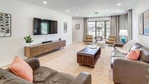 Una sala de estar moderna con un televisor de pantalla plana, sofás de cuero, una mesa de centro de madera y un amplio ventanal con cortinas.