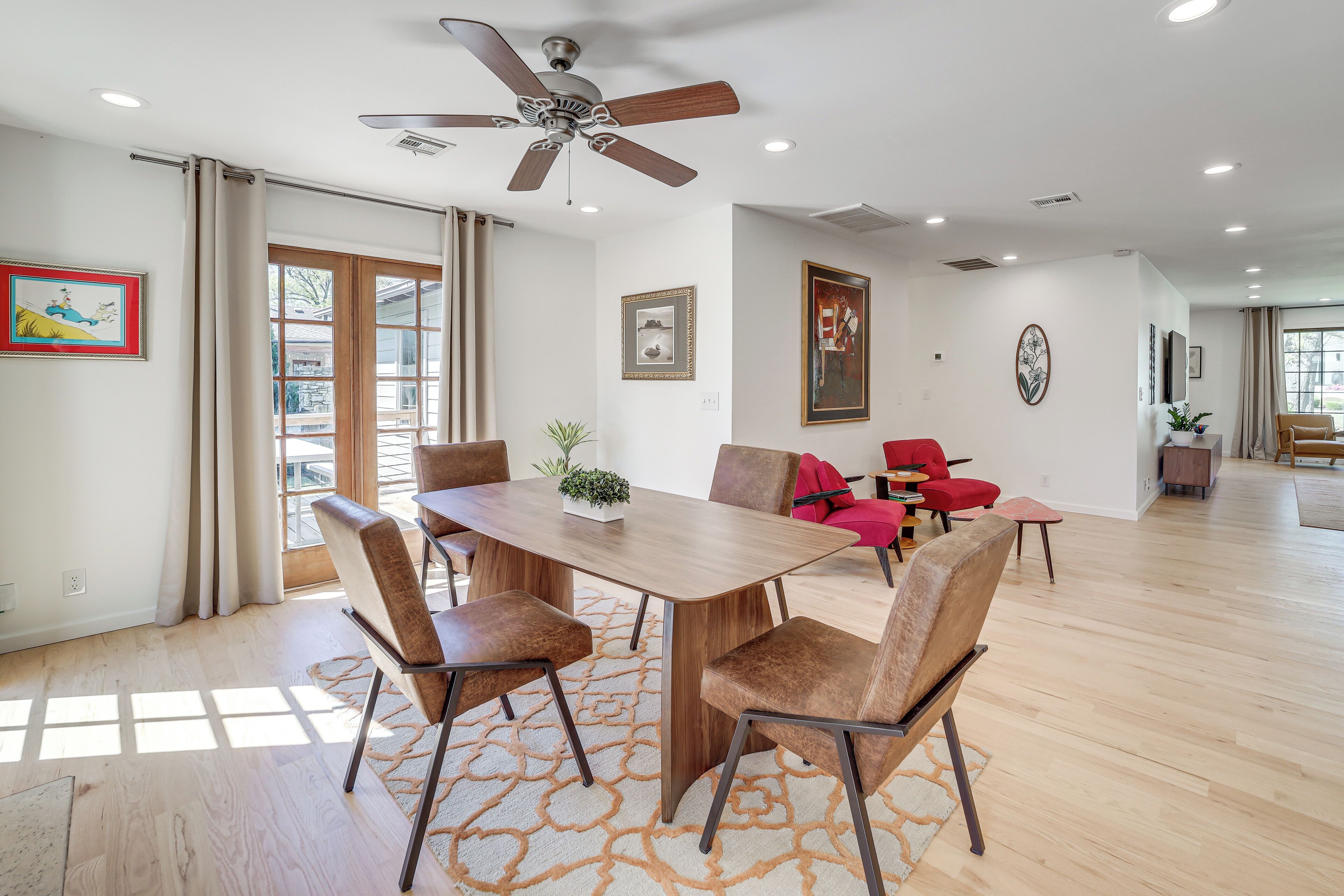 A spacious dining area with a wooden table and chairs, a ceiling fan, and a view through a glass door.