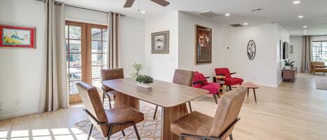 A spacious dining area with a wooden table and chairs, a ceiling fan, and a view through a glass door.